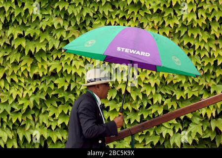 Un mayordomo se protege de la lluvia durante el día once de los Campeonatos de Wimbledon 2012 - día Once Foto de stock