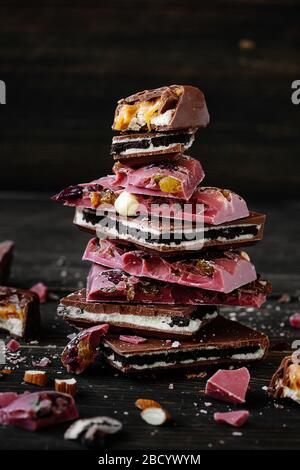 Trozos de chocolate con leche con galletas negras y chocolate rosa con nueces y pasas sobre un fondo de madera. Cerrar. Foto de stock