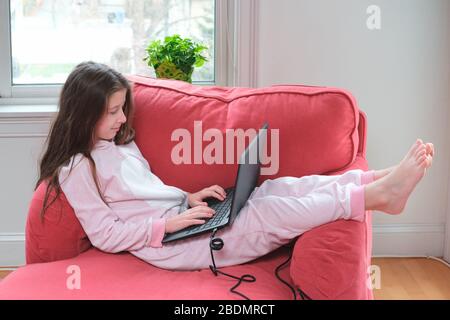 La niña preadolescente disfruta homeschooling o videollamada en un cómodo pijama y un cómodo sofá-silla. Educación remota, protección antivirus, distanciamiento social y concepto de bloqueo Foto de stock