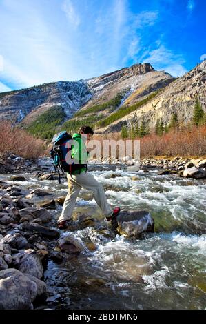 Un hombre solitario vestido con ropa colorida cruzando un rápido arroyo en las montañas rocosas de Alberta, Canadá Foto de stock