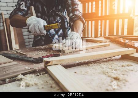 Carpintero trabajando en artesanía de madera en el taller para producir material de construcción o muebles de madera. El joven carpintero asiático utiliza herramientas profesionales para