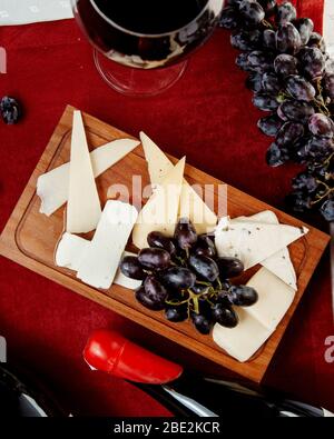 diferentes tipos de quesos y uvas y una copa de vino tinto