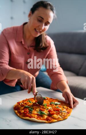 Mujer cortando una pizza tradicional italiana margarita en su sala de estar. Quédate en casa