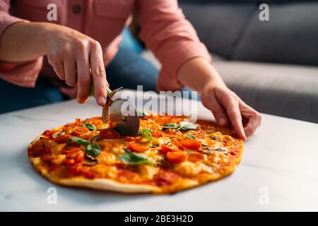 Mujer cortando una pizza tradicional italiana margarita en su sala de estar. Quédate en casa