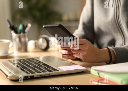 Primer plano de las manos de la niña de la estudiante que mecanografía en el teléfono inteligente sentado en un escritorio en casa por la noche Foto de stock