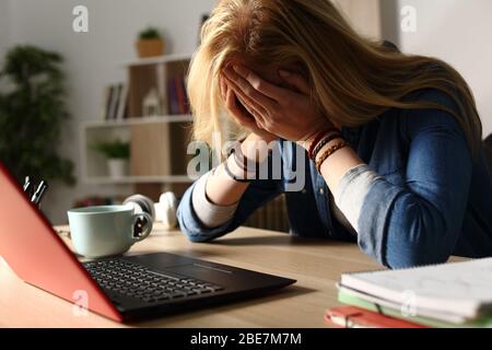 Primer plano de un estudiante triste recibiendo malas noticias en el portátil sentado en un escritorio en casa por la noche Foto de stock