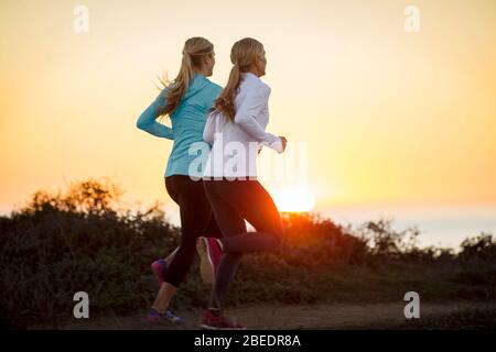 Dos jóvenes jogging junto a los acantilados junto al océano al atardecer Foto de stock
