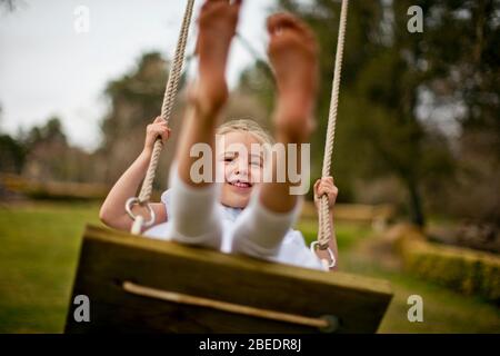 Feliz niña jugando en un columpio de cuerda de madera Foto de stock