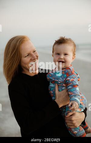 la mamá joven de la redhead ríe y sostiene niño gordo riendo de la risa en onesie