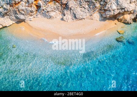 Vista aérea de playa de arena con rocas y mar con agua azul