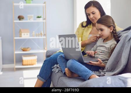 Una hermosa mujer joven y su hija están usando un ordenador portátil en casa. Foto de stock