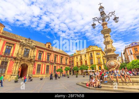 Sevilla, Andalucía, España - 18 de abril de 2016: Turistas sentados alrededor de la fuente en la Plaza Virgen de los Reyes con el palacio del Arzobispo en el fondo Foto de stock