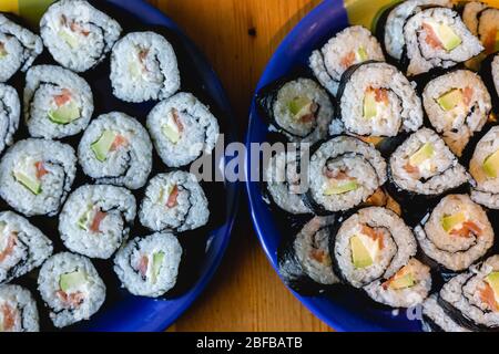 Dos platos redondos de sushi maki casero con salmón, arroz y aguacate sobre mesa de madera Foto de stock