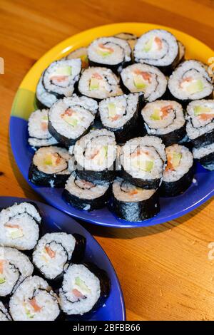 Dos platos redondos de sushi maki casero con salmón, arroz y aguacate sobre mesa de madera Foto de stock