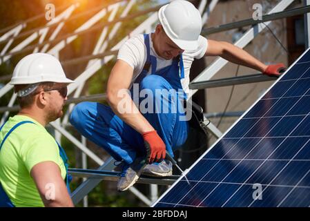 Dos técnicos profesionales instalando el panel solar fotovoltaico a la plataforma de metal con un destornillador. Instalación de sistema de panel solar independiente, eficiencia y concepto de profesionalidad. Foto de stock