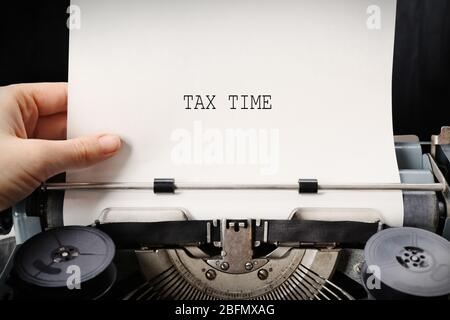 Concepto de impuestos. Mano trabajando en una máquina de escribir vieja con papel, de cerca Foto de stock