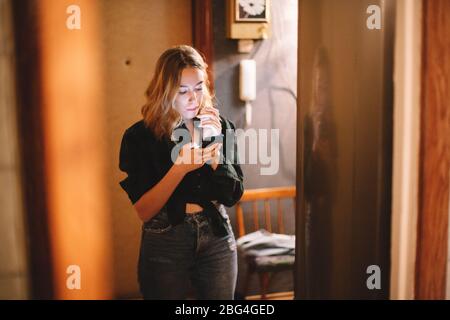Mujer joven usando el teléfono inteligente mientras está de pie junto al refrigerador en casa Foto de stock