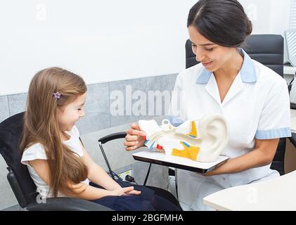Audiólogo mostrando a una niña un tímpano en el modelo del oído humano. Quejas de audición de cama en niños Foto de stock