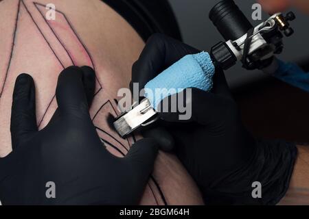 El tatuador profesional introduce tinta negra en la piel con una aguja de  una máquina de tatuajes.