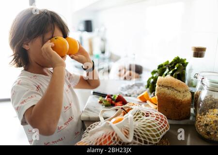 Niño en la cocina cubriendo los ojos con naranjas Foto de stock