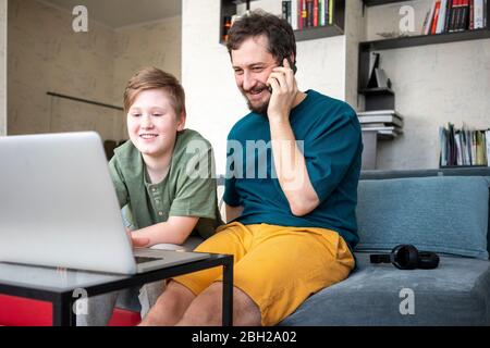 Retrato de padre e hijo sonriendo sentados juntos en el sofá mirando al portátil