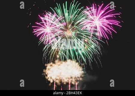 Fuegos artificiales verdes y púrpura a mitad de la explosión contra un cielo nocturno oscuro