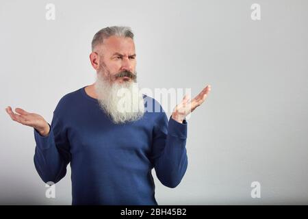 Retrato de un hombre de pelo gris maduro indignado sobre fondo gris, enfoque selectivo Foto de stock