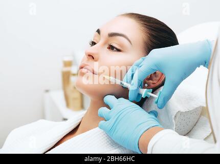 el médico con una jeringa de toxina botulínica llena una arruga cerca de la boca para rejuvenecer la piel Foto de stock