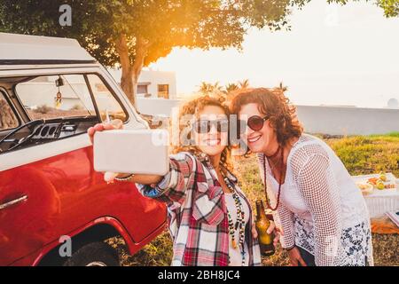 Agradable atractivo par de mujeres de edad media viajar junto con la vieja vendimia de la furgoneta roja y tomar selfie con teléfono moderno durante la actividad de ocio al aire libre del picnic - día soleado de vacaciones de verano