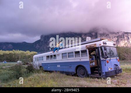 dos personas sentadas en la parte superior del autobús escolar leyendo libro frente a la montaña