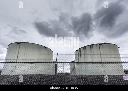 Depósitos de combustible de chorro grandes o de almacenamiento de aceite detrás de una valla de eslabón de cadena con señales de advertencia. Foto de stock