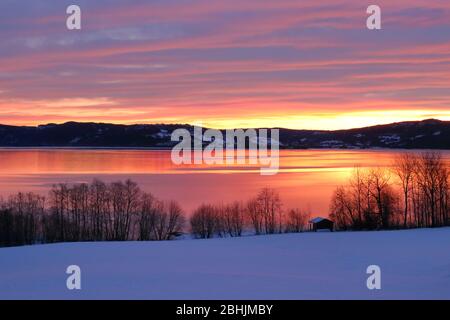 Vista panorámica de una increíble puesta de sol de invierno reflejada en el tranquilo lago Selbusjøen, Selbustrand, Noruega