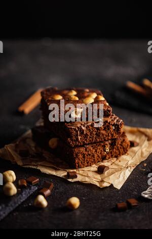 Pastel de chocolate negro y brownie de cacao sobre mesa de concreto gris claro, trozos de chocolate y avellanas Foto de stock