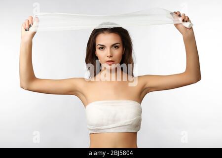 Mujer joven y hermosa con un vendaje en el pecho, sosteniendo una gasa, aislada sobre blanco Foto de stock