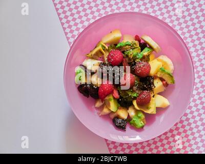 Ensalada de frutas frescas veganas en un tazón rosa: Aguacate, frambuesas, manzana, plátano, ciruelas, bayas de goji y semillas de chía Foto de stock