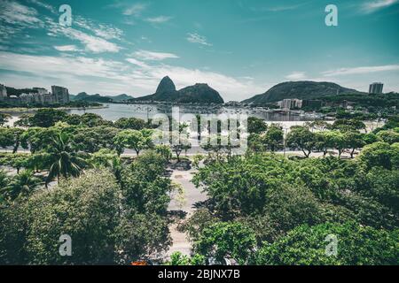 Tiro aéreo de gran angular de un distrito de Botafogo de Río de Janeiro, Brasil con múltiples palmeras y otros árboles tropicales en primer plano, una bahía detrás Foto de stock