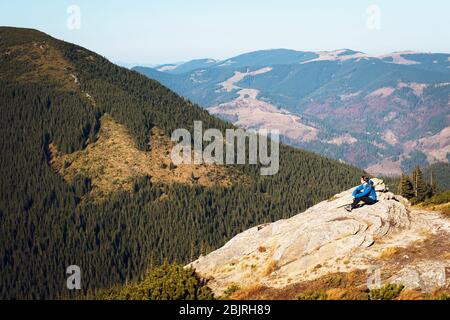 Vista lateral de mujer caminante sentada en la roca en la cima de la colina mientras mira el paisaje de las montañas. Montañas Cárpatos, Ucrania. Concepto de senderismo