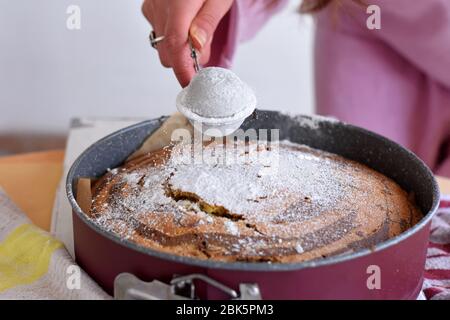 La mano de la mujer roció azúcar glaseado sobre pastel de mármol fresco. El azúcar en polvo cae sobre una tarta de mármol recién horneada Foto de stock