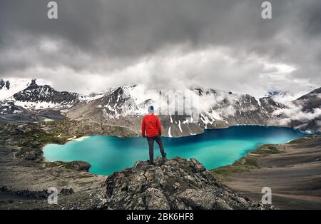 Hombre de chaqueta roja está buscando Ala-Kul lago en las montañas Tien Shan, con blancas nubes de niebla en Karakol, parque nacional de Kirguistán