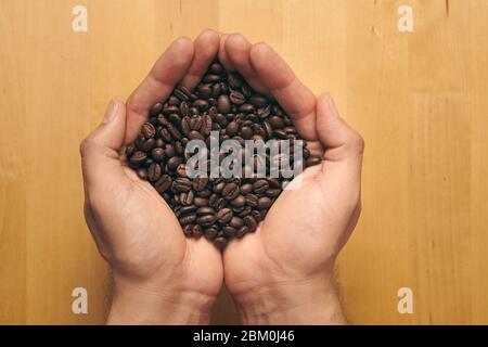 Un puñado de granos de café recién molidos sobre un fondo de madera Foto de stock