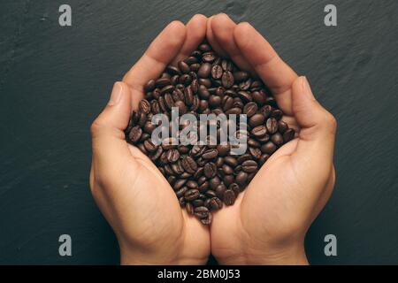 Un puñado de granos de café recién molidos sobre una pizarra de piedra oscura Foto de stock