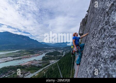 Hombre mirando hacia arriba mientras escalaba en roca Squamish Chief sobre granito con vista Foto de stock