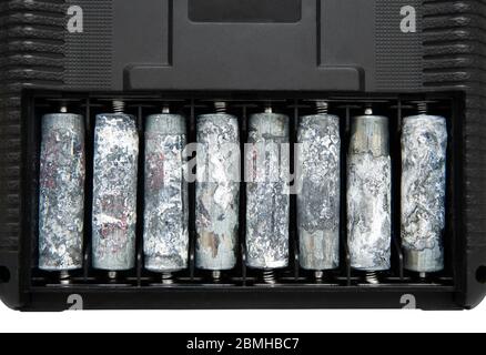 Una fila de ocho pilas AA sin envolver y muy oxidadas dentro del compartimento de las pilas de un dispositivo electrónico. Foto de stock