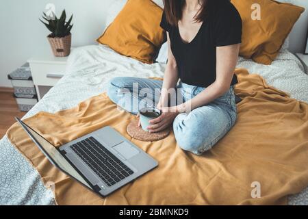 Mujer joven relajante y beber taza de café caliente o té utilizando el ordenador portátil en bedroom.woman comprobar las aplicaciones sociales y el trabajo.