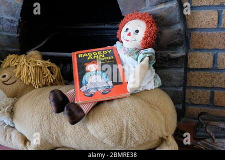 Raggedy Ann muñeca sentada por una chimenea con una reimpresión de 1961 del libro Raggedy Ann Stories por Johnny Gruel en su regazo; trapo muñeca. Foto de stock