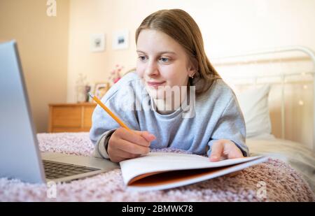 Niña adolescente Lying en la cama en el dormitorio con portátil estudiando y la escuela en casa Foto de stock