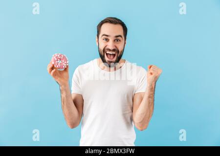 Imagen de joven emotivo hombre aislado sobre fondo azul pared sosteniendo donut. Foto de stock