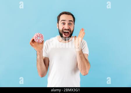 Imagen de joven emotivo hombre aislado sobre fondo azul pared sosteniendo donut. Foto de stock
