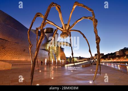 Araña gigante de bronce entre el río y el Museo Guggenheim Bilbao por la noche