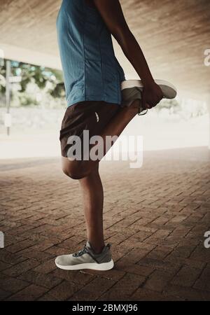 Sección baja de un estilo de vida saludable hombre afroamericano estirando las piernas antes de correr en la calle de la ciudad